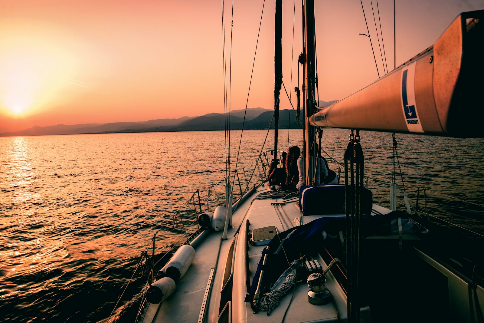 Velero navegando al atardecer con dos personas sentadas en la proa