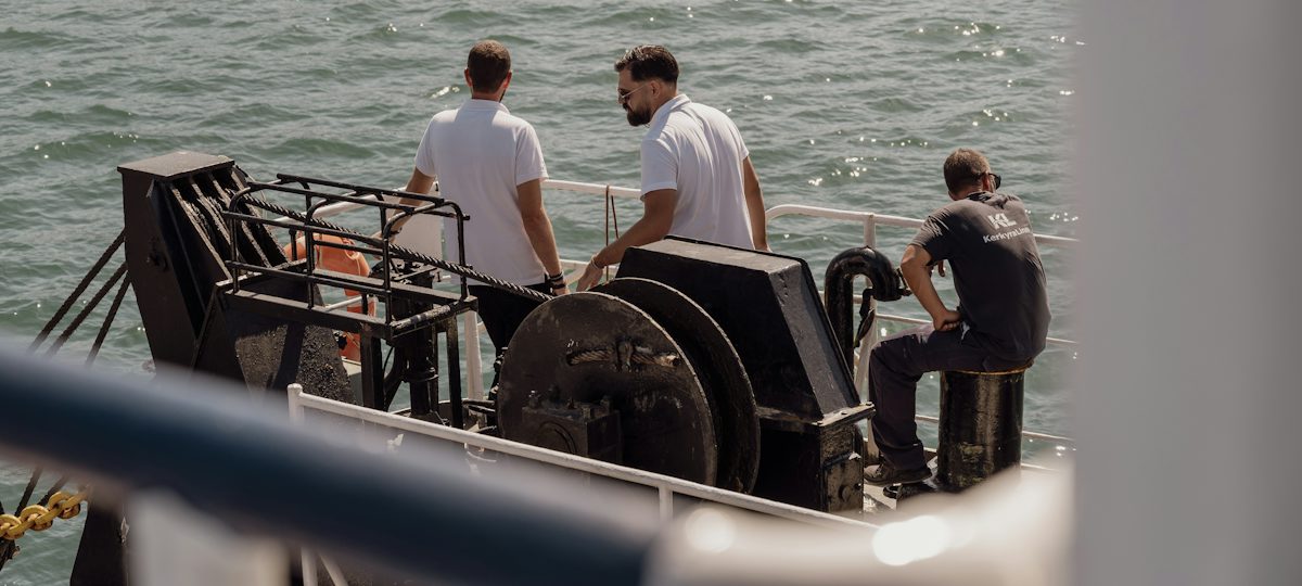 Tres personas en la cubierta de un velero mirando el mar