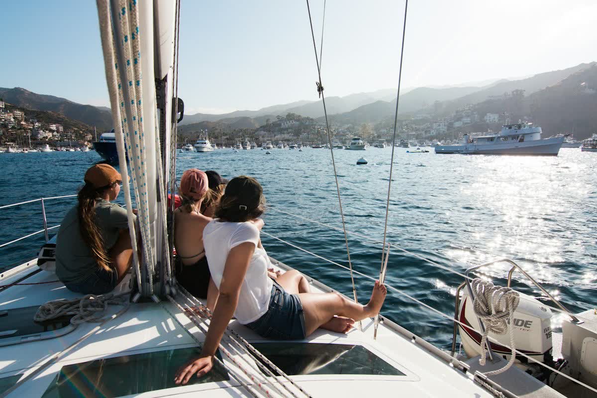Cuatro personas sentadas en la cubierta de un velero, mirando una bahía con barcos fondeados